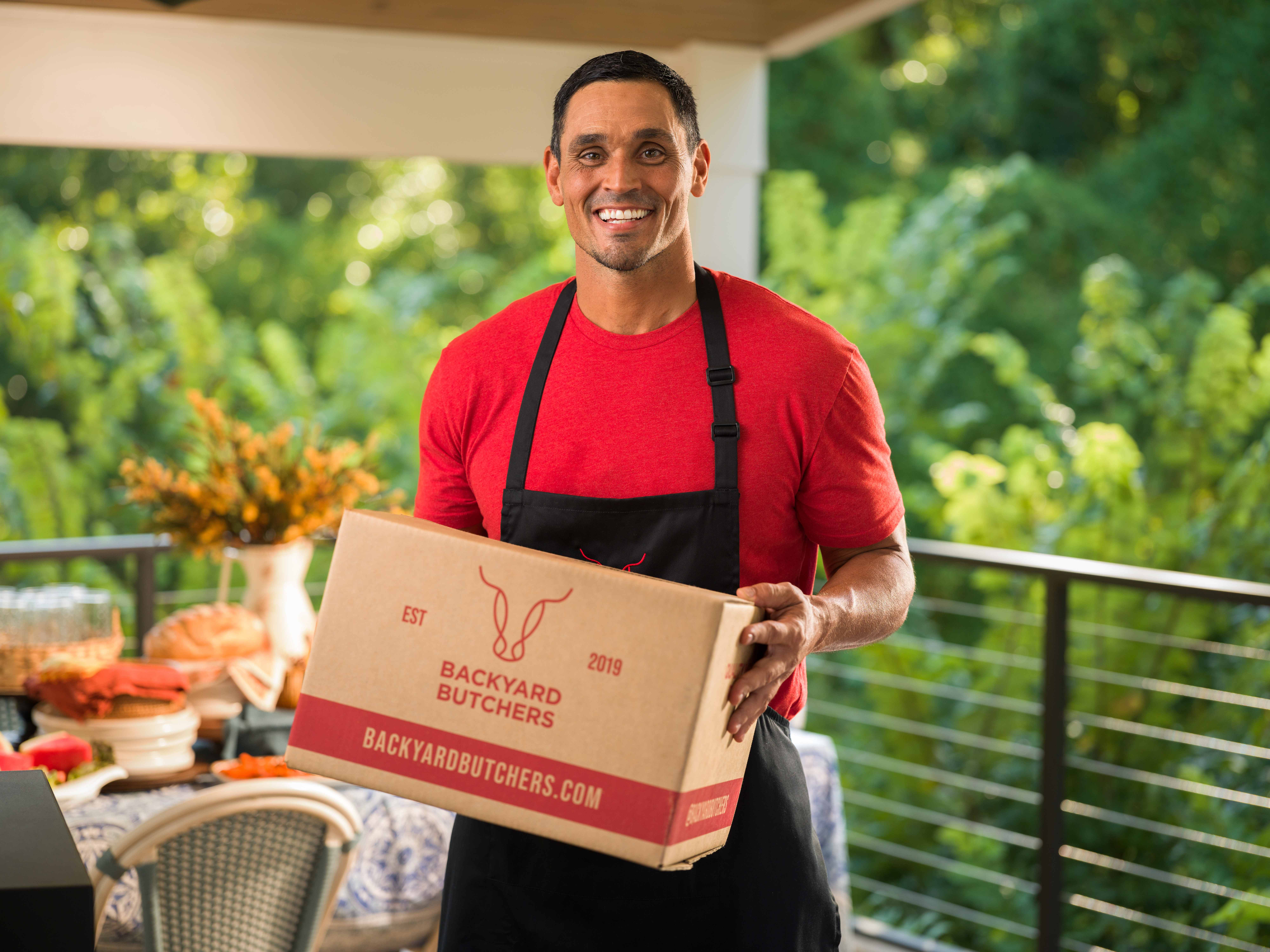 David Pollack — David on the patio in a red tee and apron, holding a Backyard Butchers box.