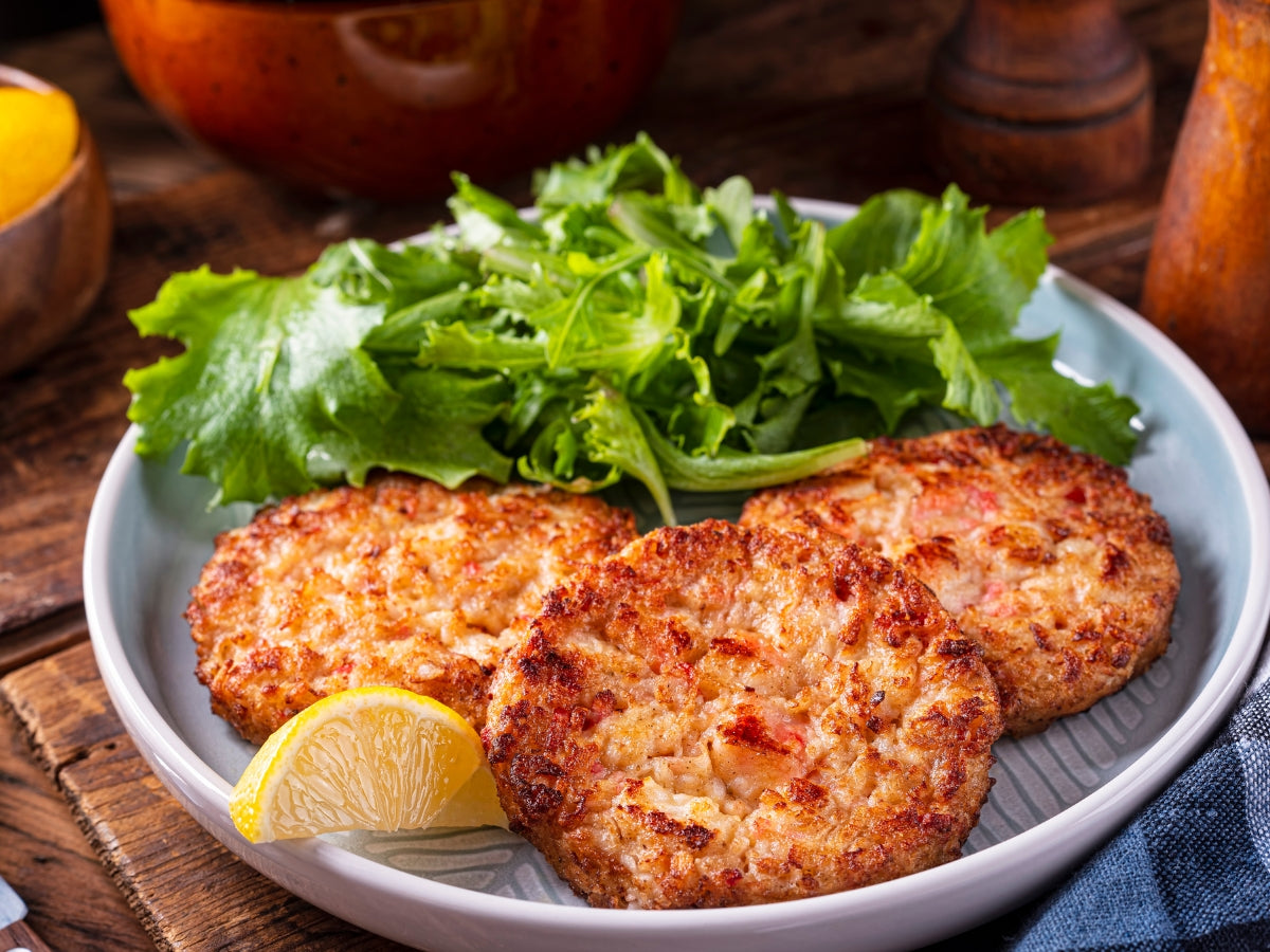 Golden crab cakes plated with fresh greens and a lemon wedge