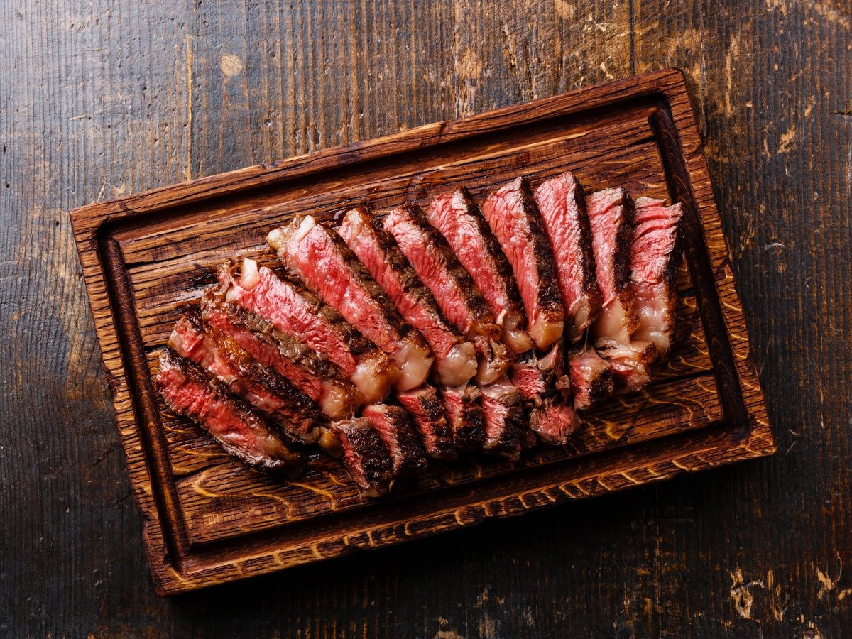 Sliced, grilled steak fanned out on a wooden cutting board